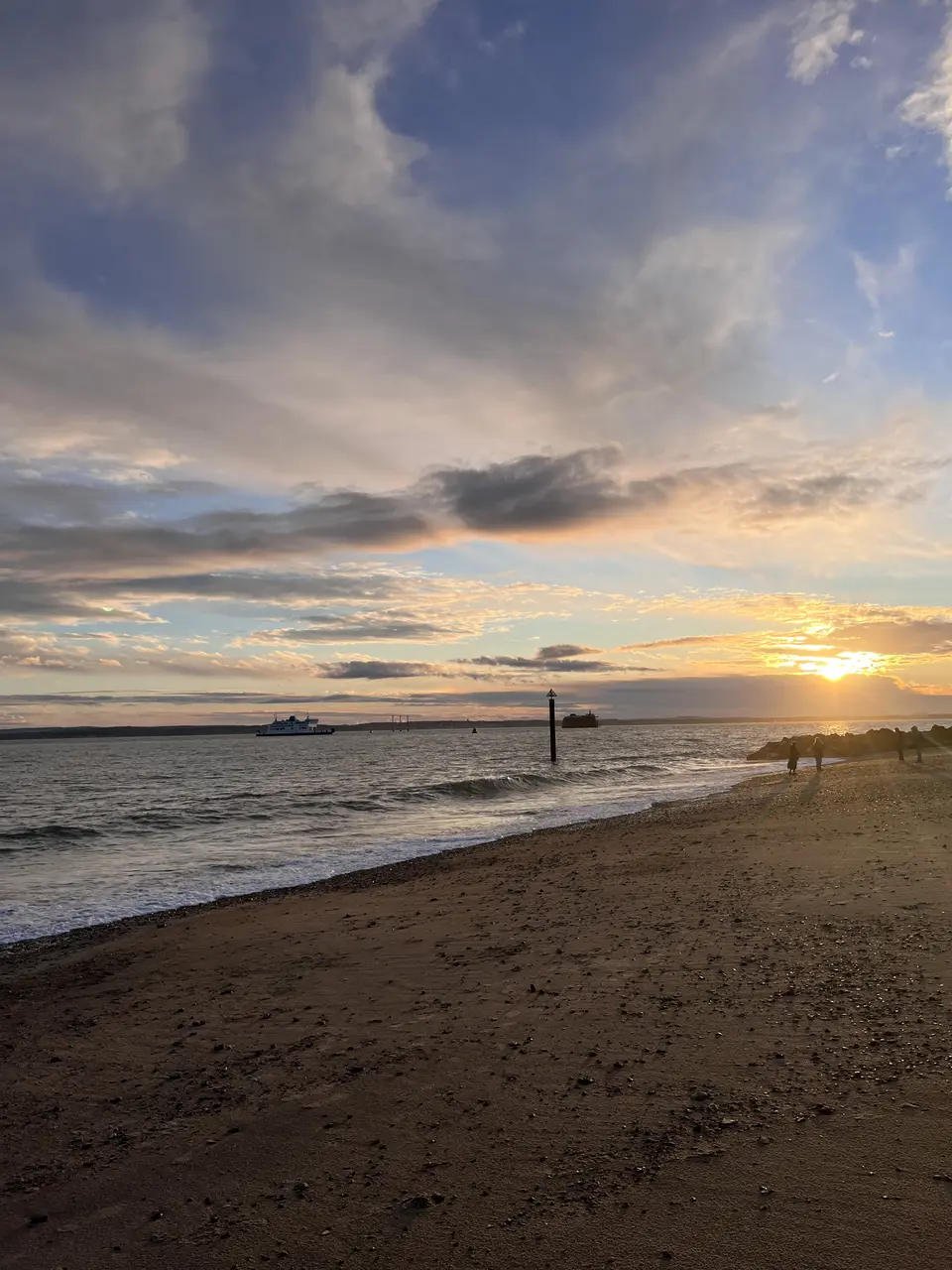 A wide sandy beach at sunset with a ferry on the horizon and broken cloud catching the light
