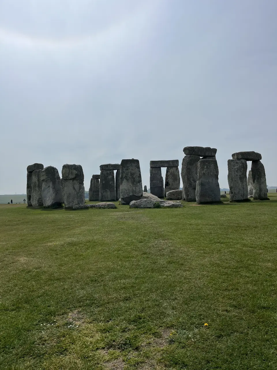 The standing stones of Stonehenge under a pale overcast sky, surrounded by open grassland